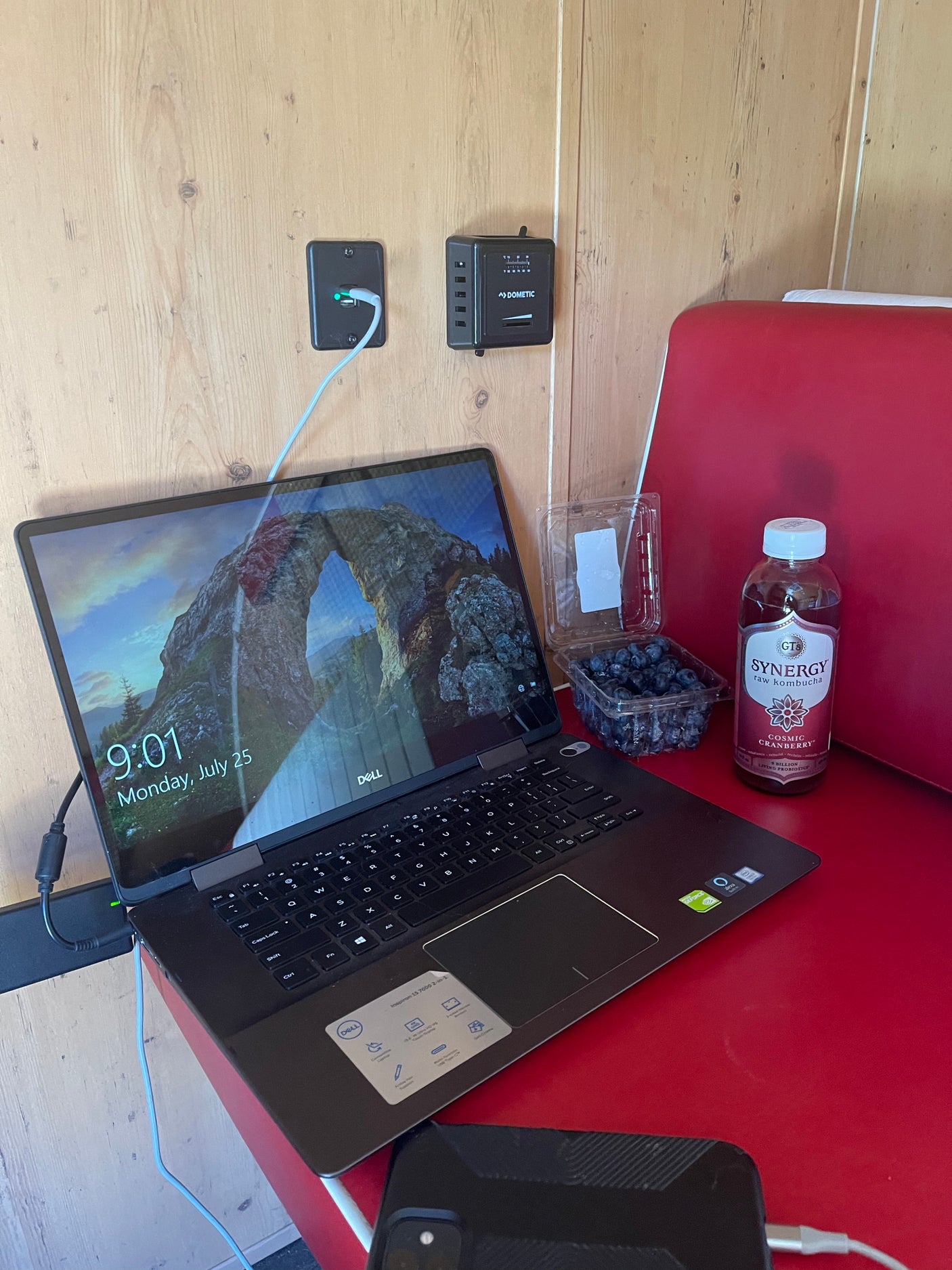 RV rental setup: Dell laptop, Dometic controls, kombucha, and blueberries on a red table, showing a mobile workspace.