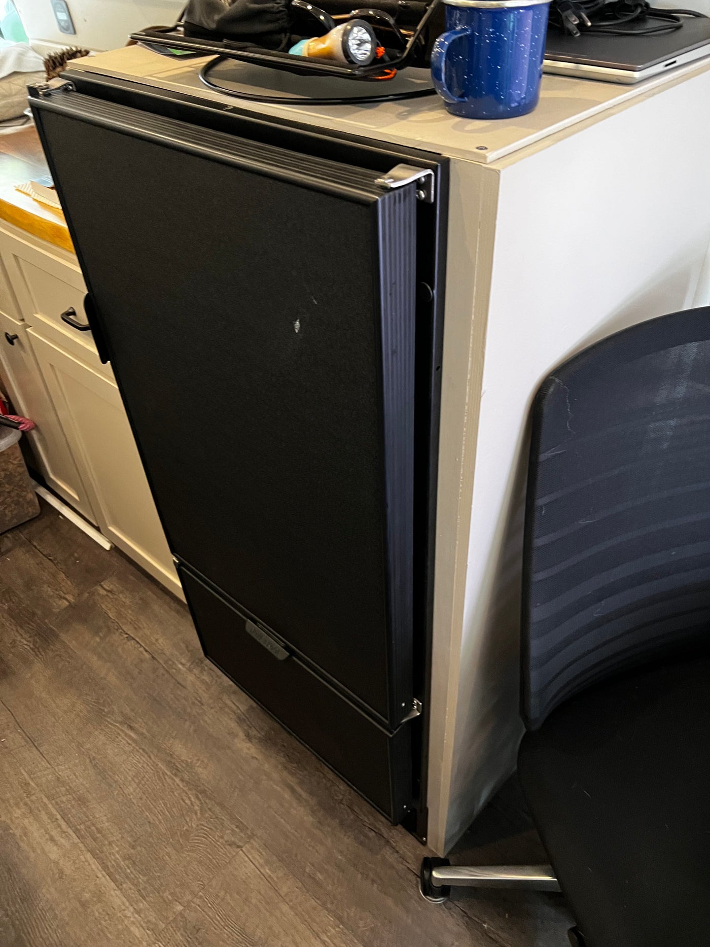 Black portable fridge/freezer, partially open, with blue mug & electronics on top, in an rv rental setting. Practical RV living. — photo 9