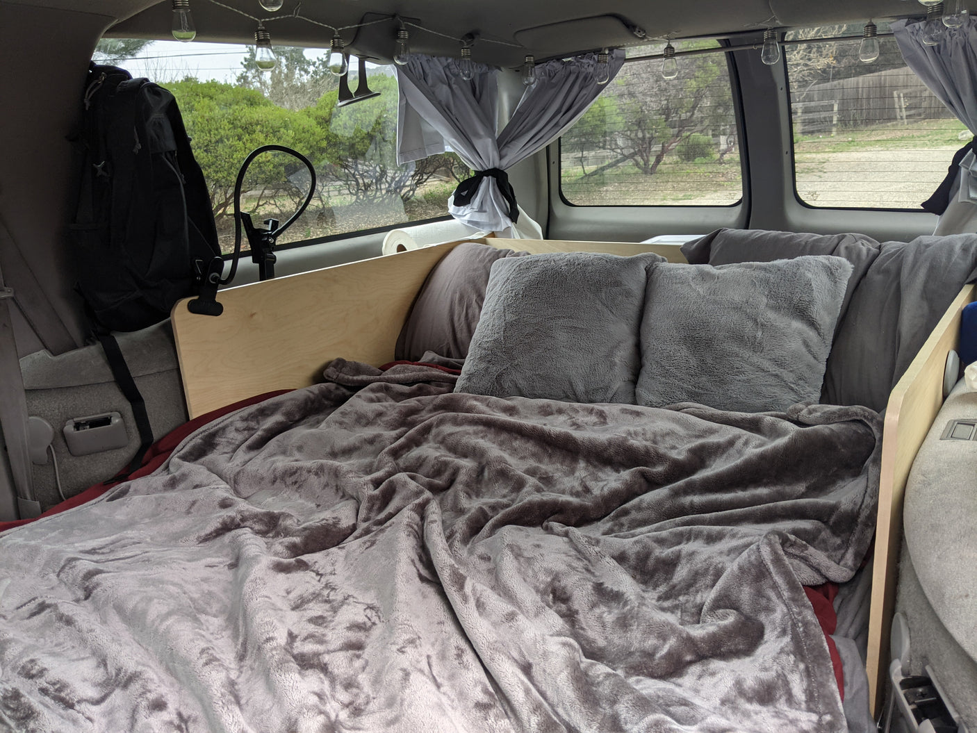 RV rental: Comfortable camper van bed with fluffy blankets, pillows, and charming string lights for a cozy night.