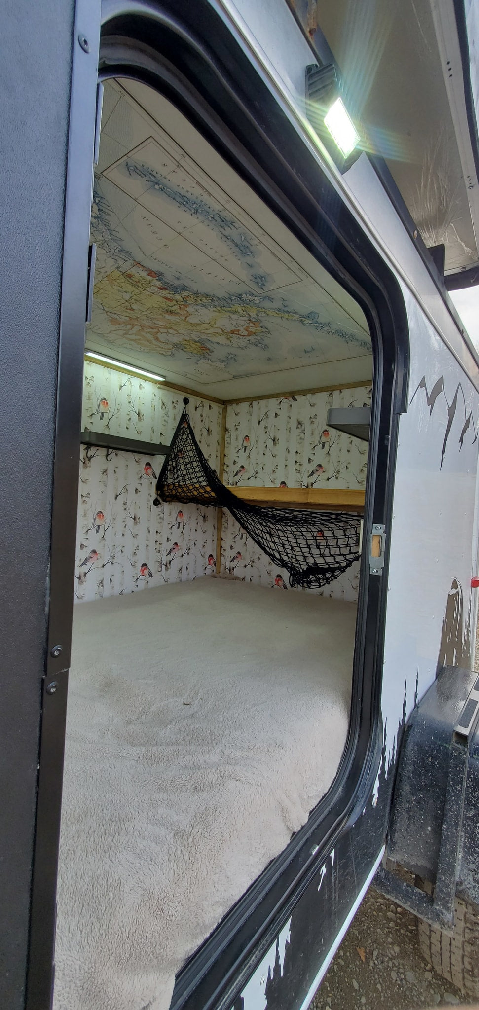RV rental: Inside this cozy camper, a map lines the ceiling, bird walls, a soft bed, and a storage net.