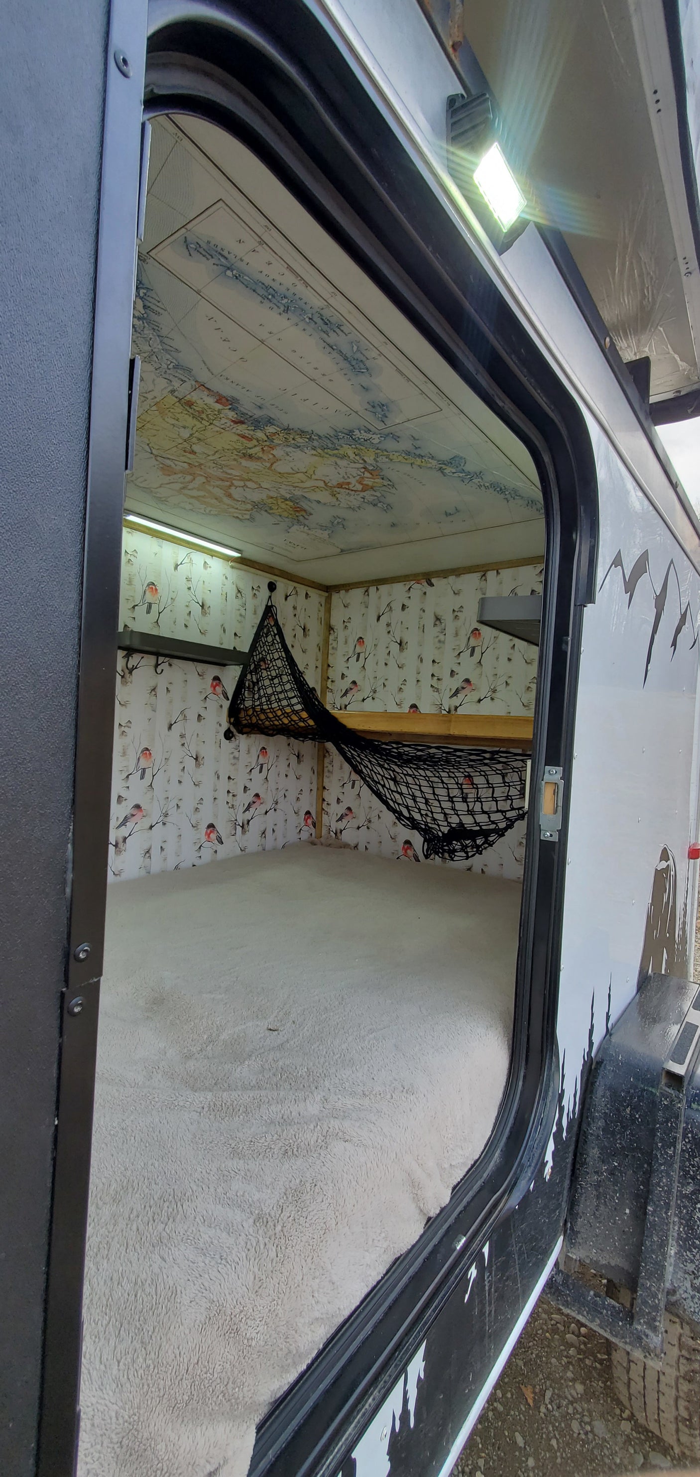 RV rental: Inside this cozy camper, a map lines the ceiling, bird walls, a soft bed, and a storage net.