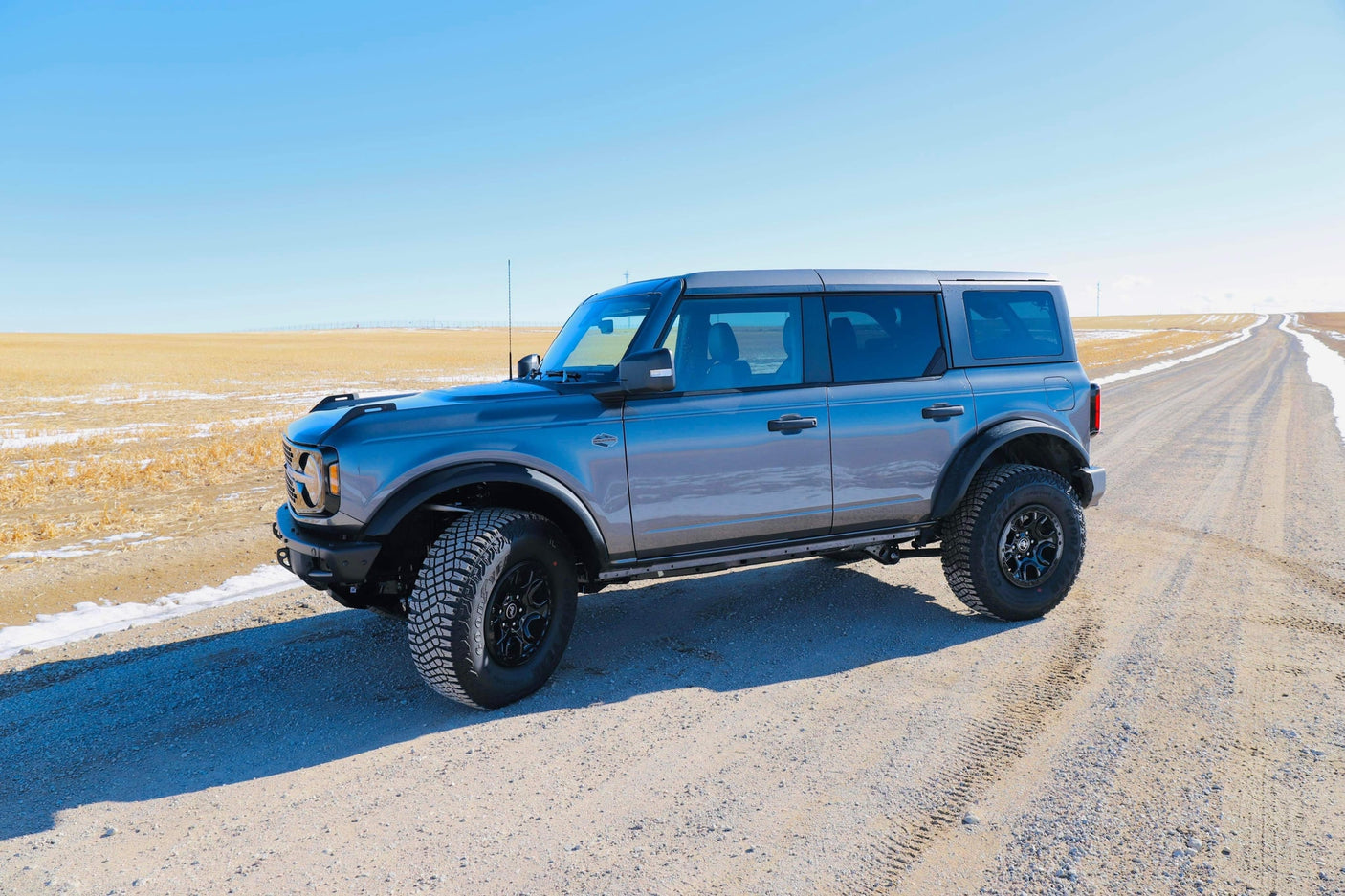 A gray Ford Bronco SUV on a dirt road by open fields under a blue sky, perfect for your next rv rental adventure.