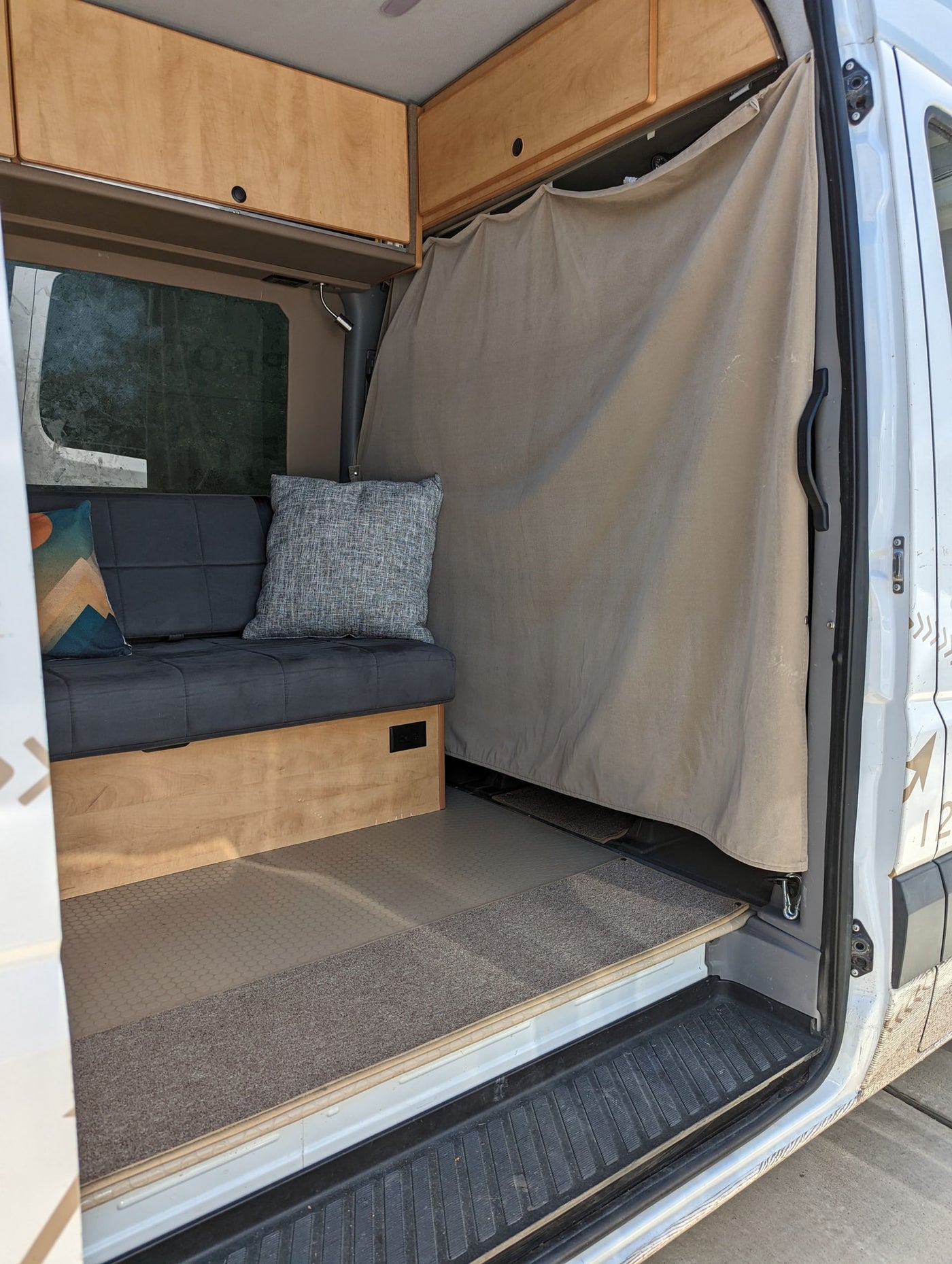 Camper van interior with a bench seat, wooden overhead cabinets, and a privacy curtain, ready for your rv rental adventure. — photo 10