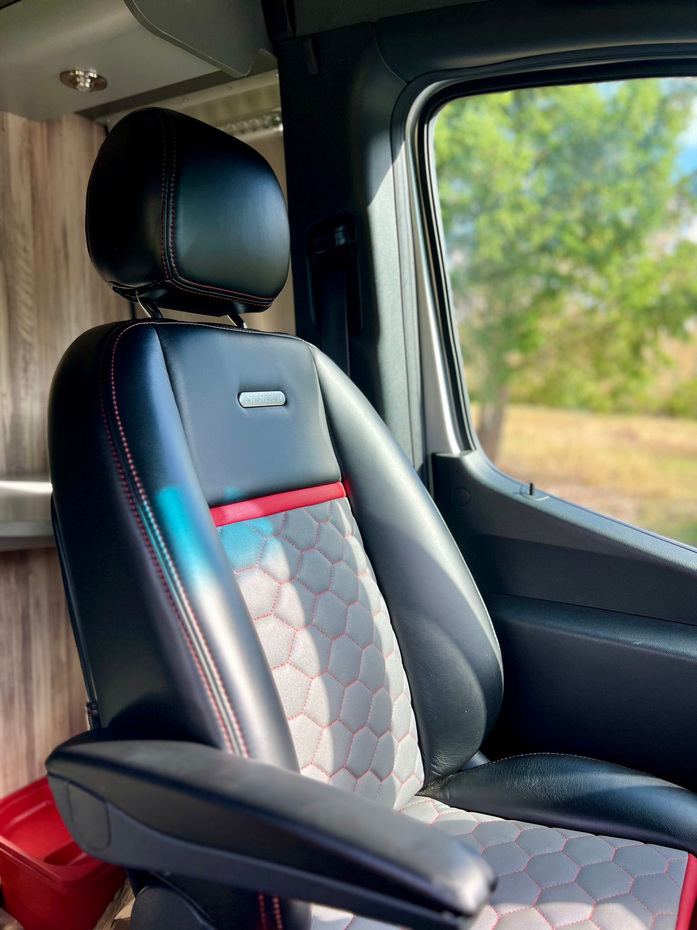 Inside an RV rental: stylish black and gray Airstream seat with red stitching. A scenic window view suggests travel and comfort.