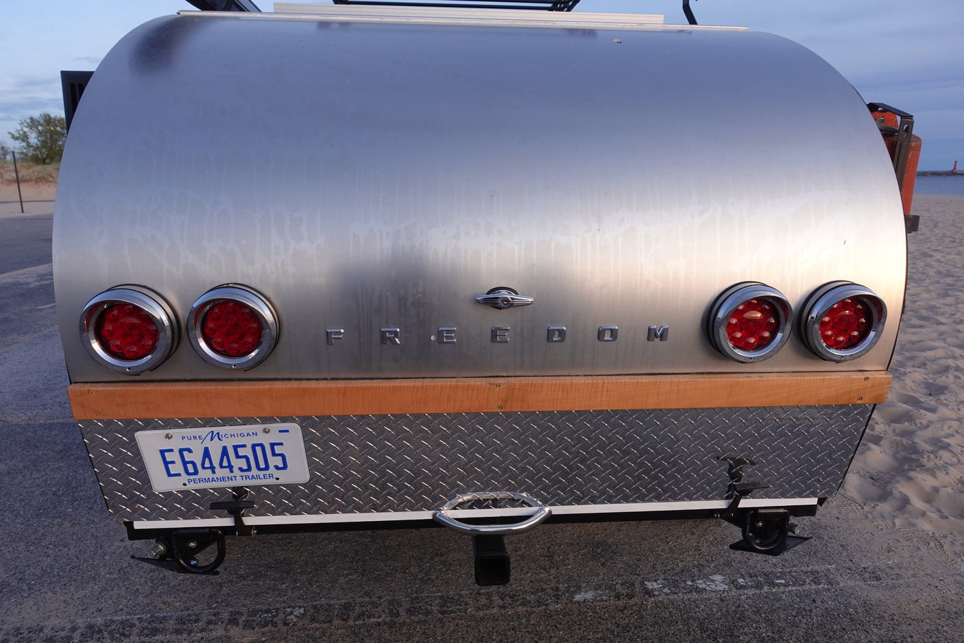 Rear view of a silver "Freedom" teardrop RV rental, Michigan plate E644505. Ready for adventure by the beach.