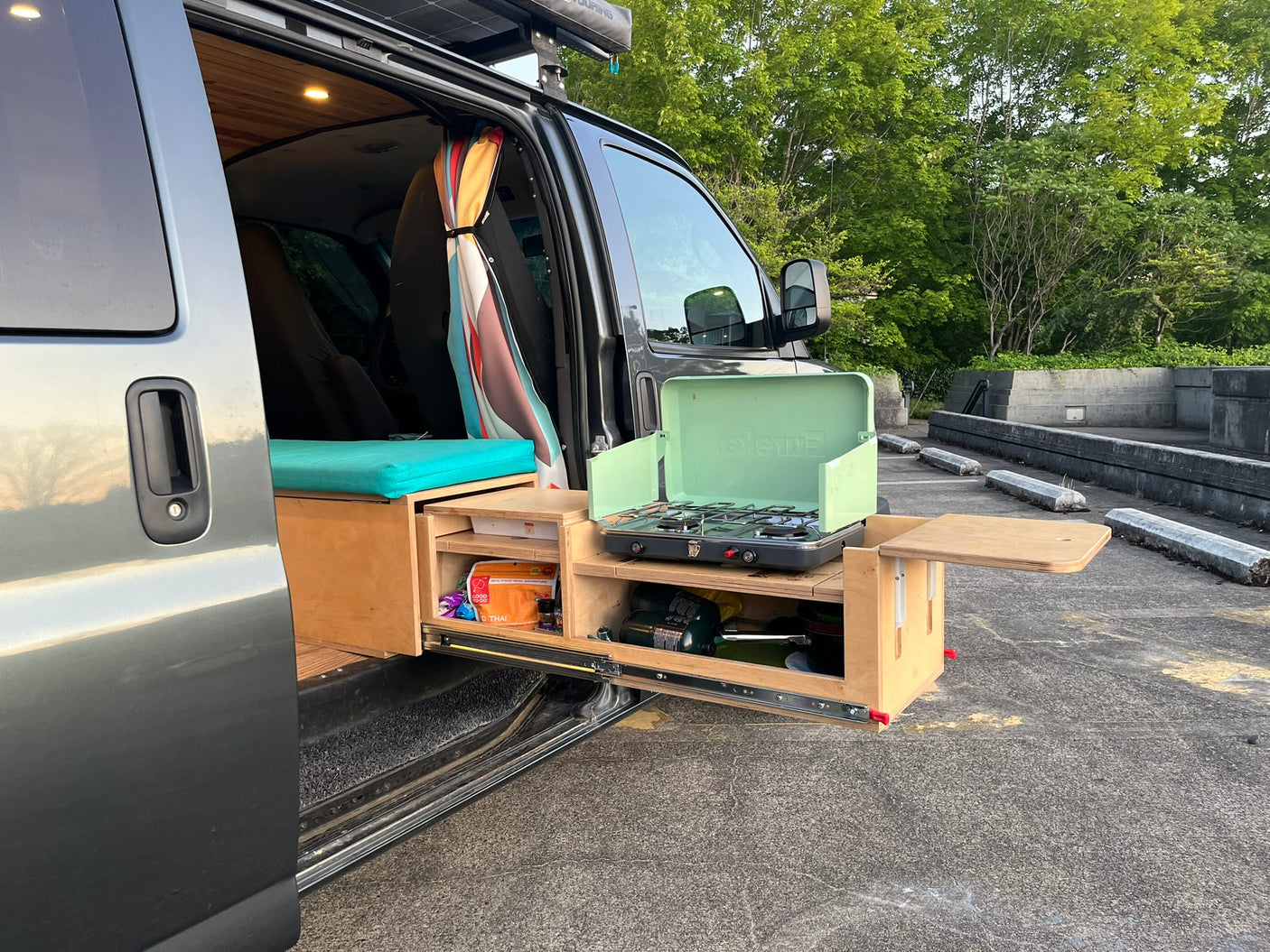 Open side door of an RV rental reveals a custom interior & a pull-out outdoor kitchen with a gas stove.