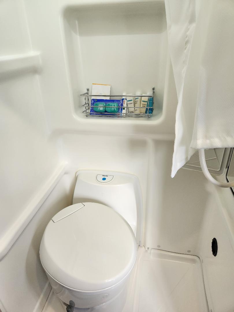 Explore your RV rental's compact wet bath, featuring a toilet, shower area with curtain, and convenient wall-mounted toiletries.