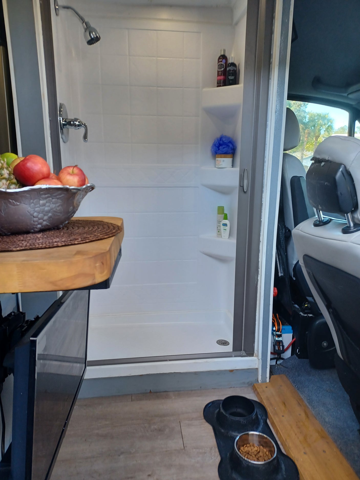 This RV rental interior features a functional shower, dog food station, TV, and fruit, offering comfort on the road.