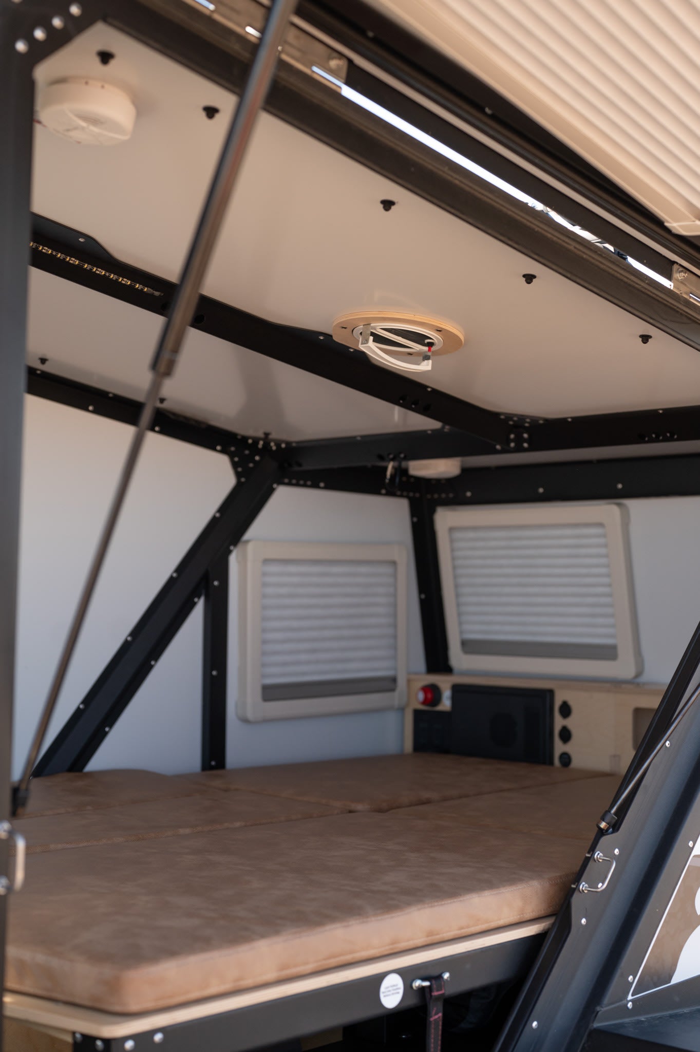 Cozy RV rental interior with a comfortable bed, small windows, and an overhead fan, ready for your next adventure.
