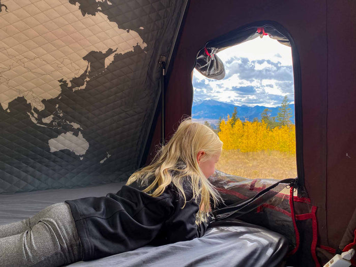 drives on a dirt road through a vast desert landscape with snow-capped mountains.|SUV's open rear for overlanding: full kitchen