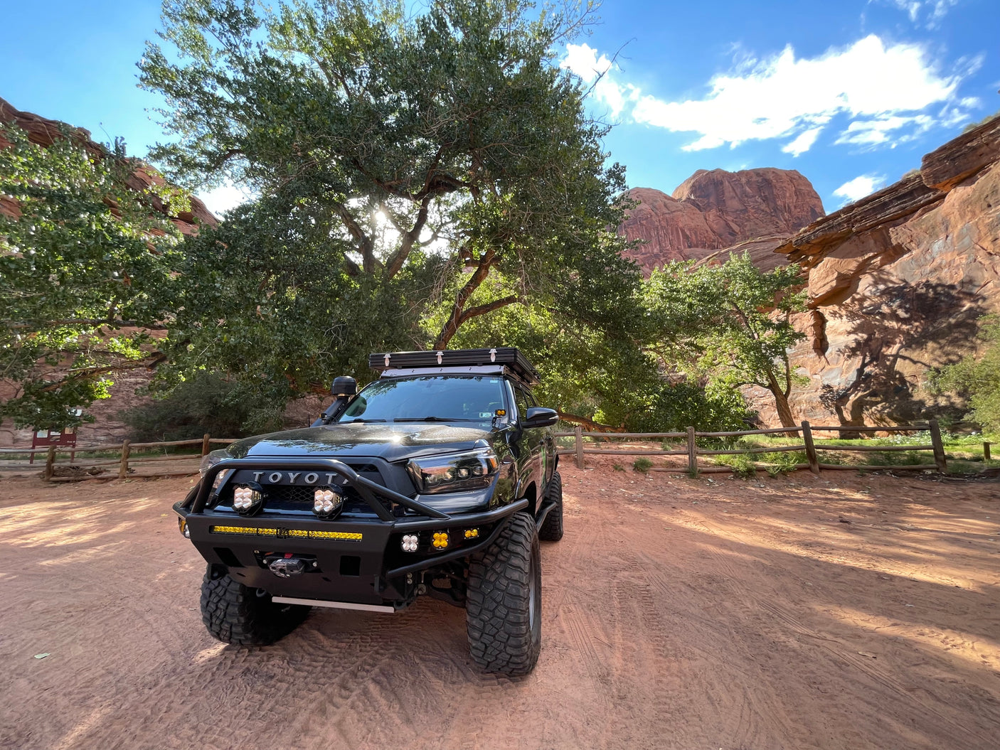 Rugged black Toyota 4Runner, an ideal RV rental for off-road adventures, parked by vibrant trees & stunning red rock cliffs.