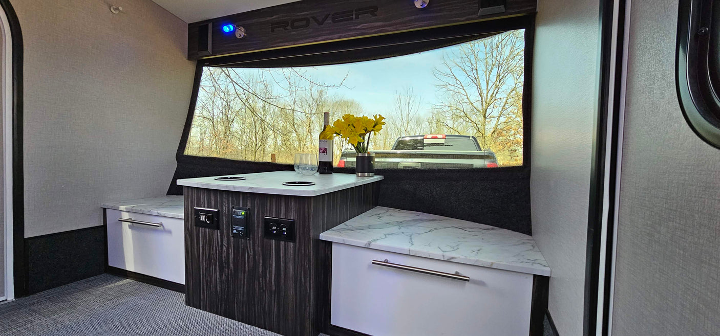 RV rental interior: Cozy space with a central table, bench seating, wine, flowers & a large window view.