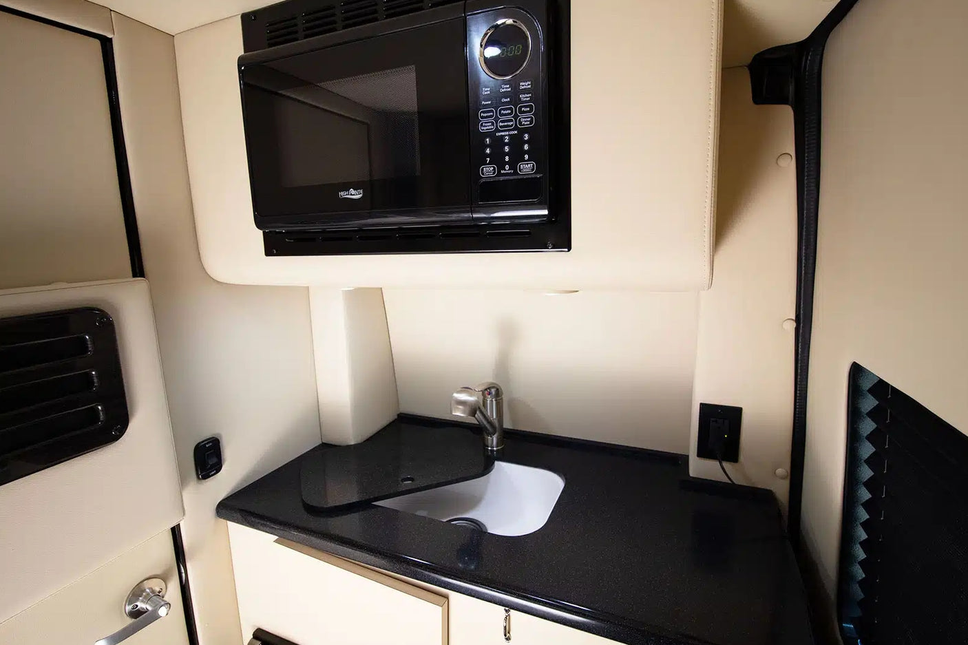 This RV rental features a compact kitchenette with a black microwave mounted above a dark countertop, sink, and faucet.