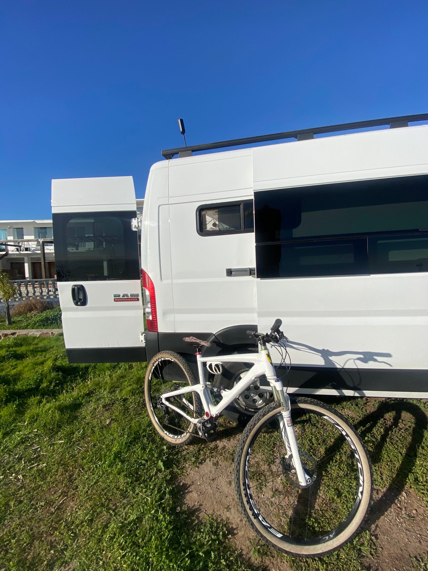 White RV rental van with its back doors open, and a white mountain bike parked outside on the grass, ready for an adventure.