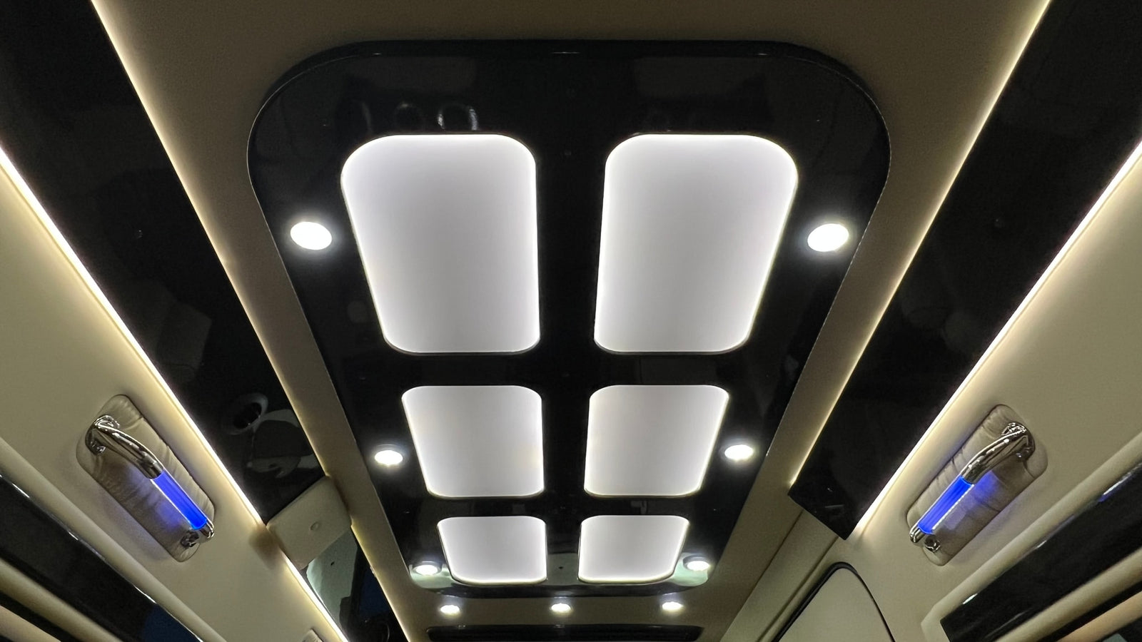 Luxury RV rental ceiling showcases modern design: bright white panel lights, accent lights, and blue ambient grab handles.