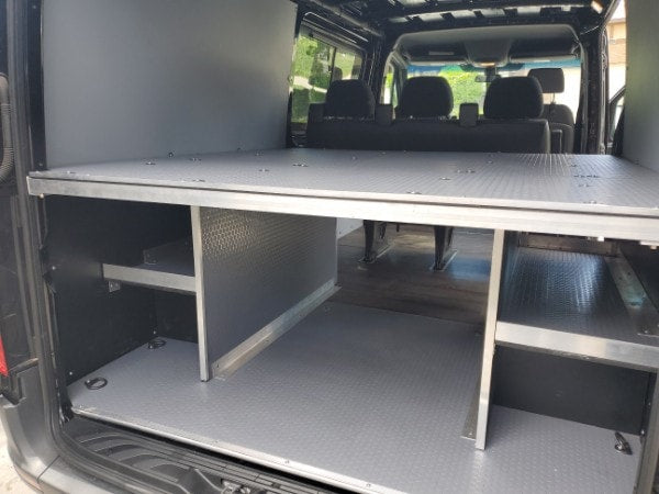 Spacious RV rental interior with an elevated bed platform and organized storage compartments for gear and supplies.|RV rental van interior with three black passenger seats
