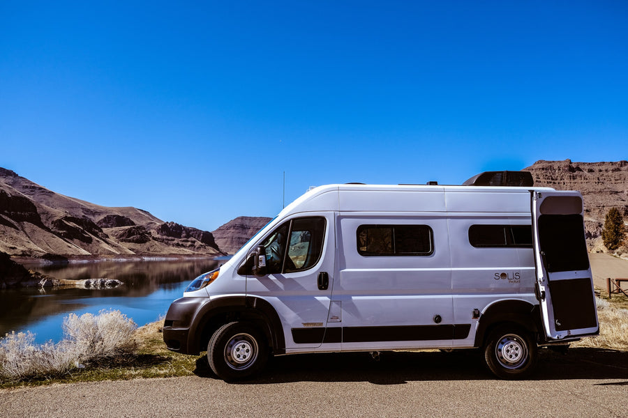 This rv rental, a white Solis Pocket camper van, is parked by a scenic lake with mountains, perfect for adventure.