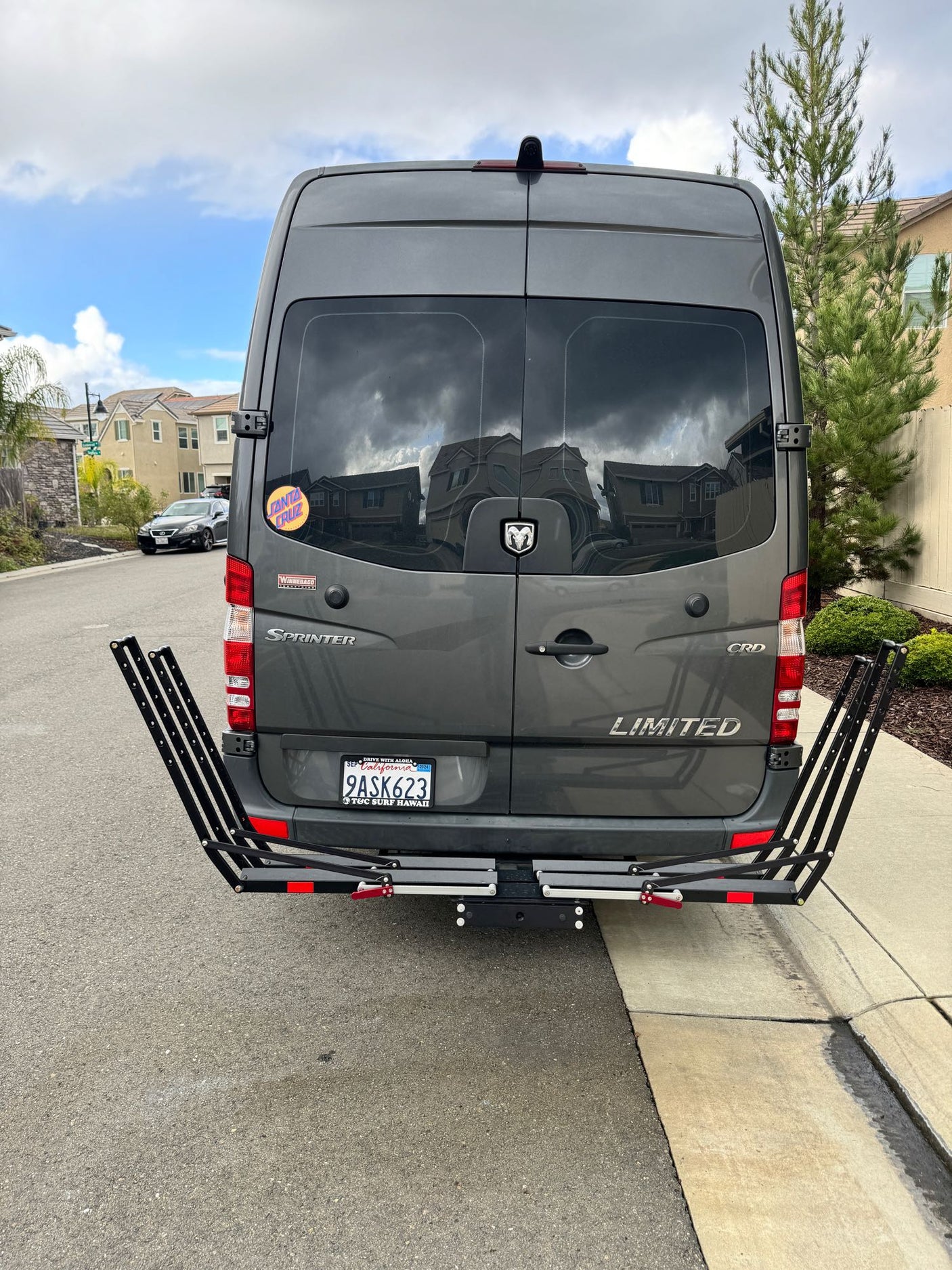 Gray Winnebago Sprinter van, an ideal RV rental, with rear carrier rack parked on a residential street.