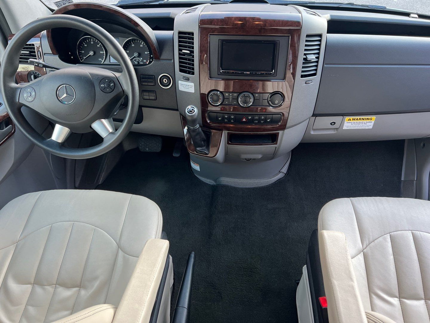 **RV rental**: Front cabin view with Mercedes-Benz steering wheel, wood-trimmed dashboard, and light-colored seats.