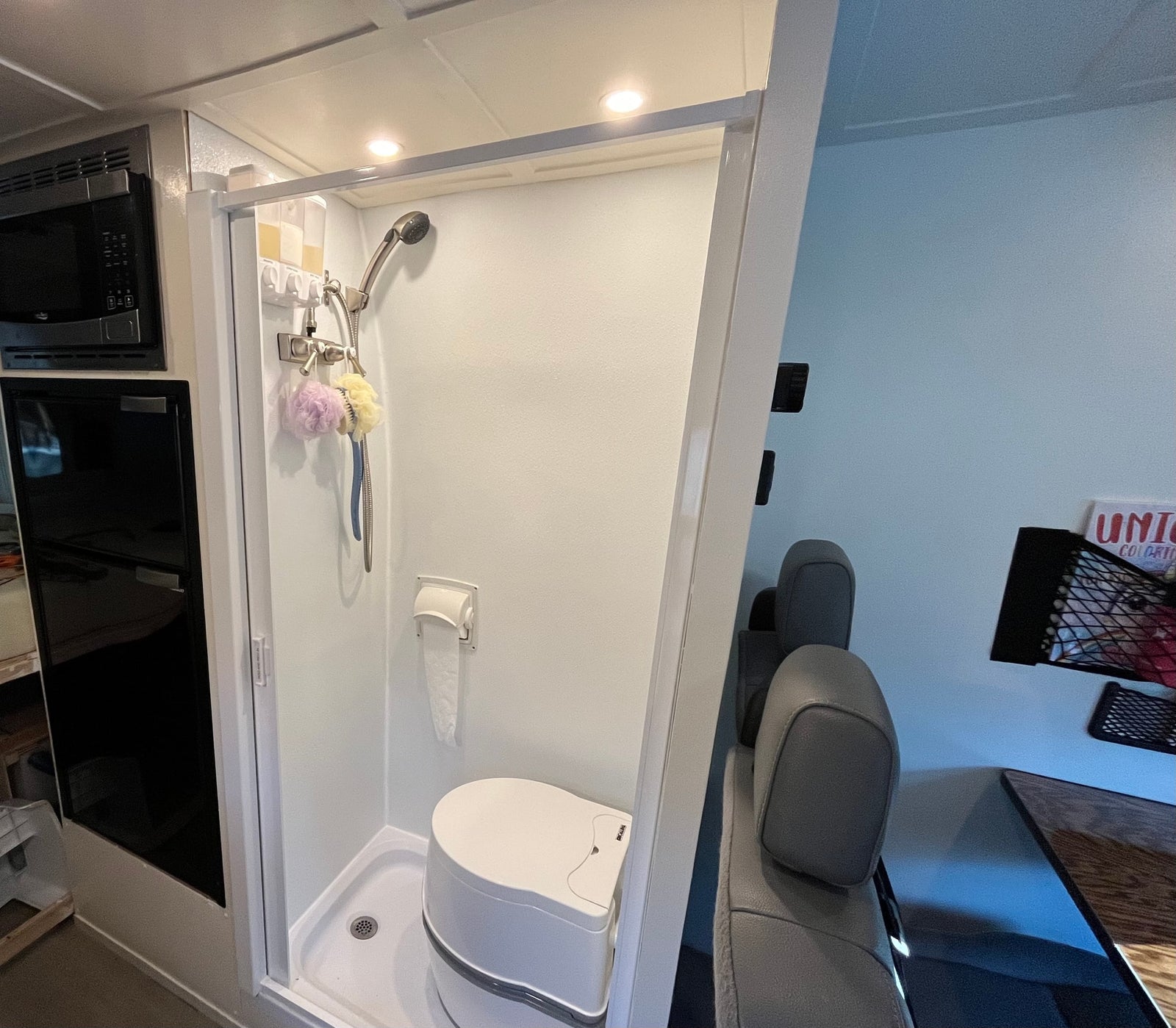 RV rental interior: compact wet bath with shower and portable toilet. Adjacent microwave and mini-fridge.