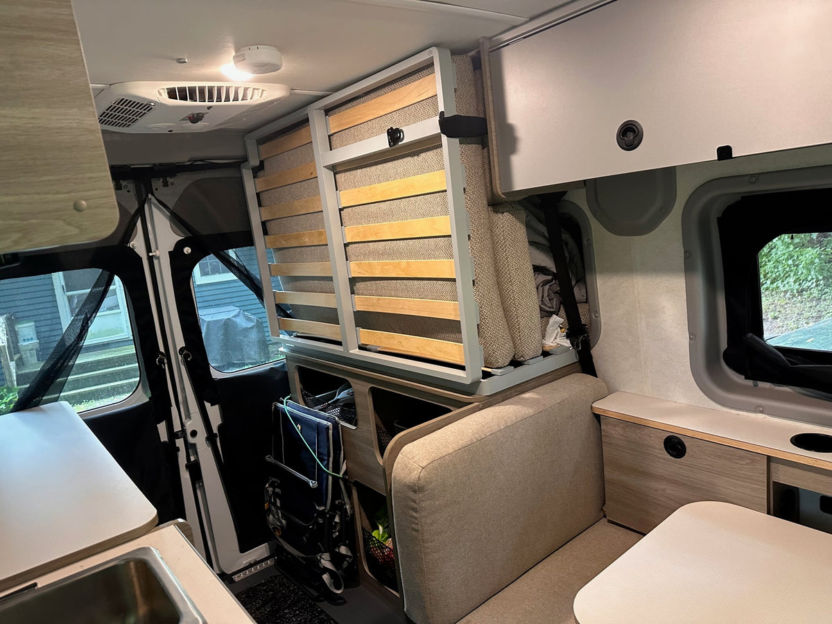 and laptop workspace with forest views.|White rv rental with door open & table out. Wooden stairs lead to a beach pier where two people are fishing by the ocean.|Spacious rv rental interior showing sleeping areas — photo 15