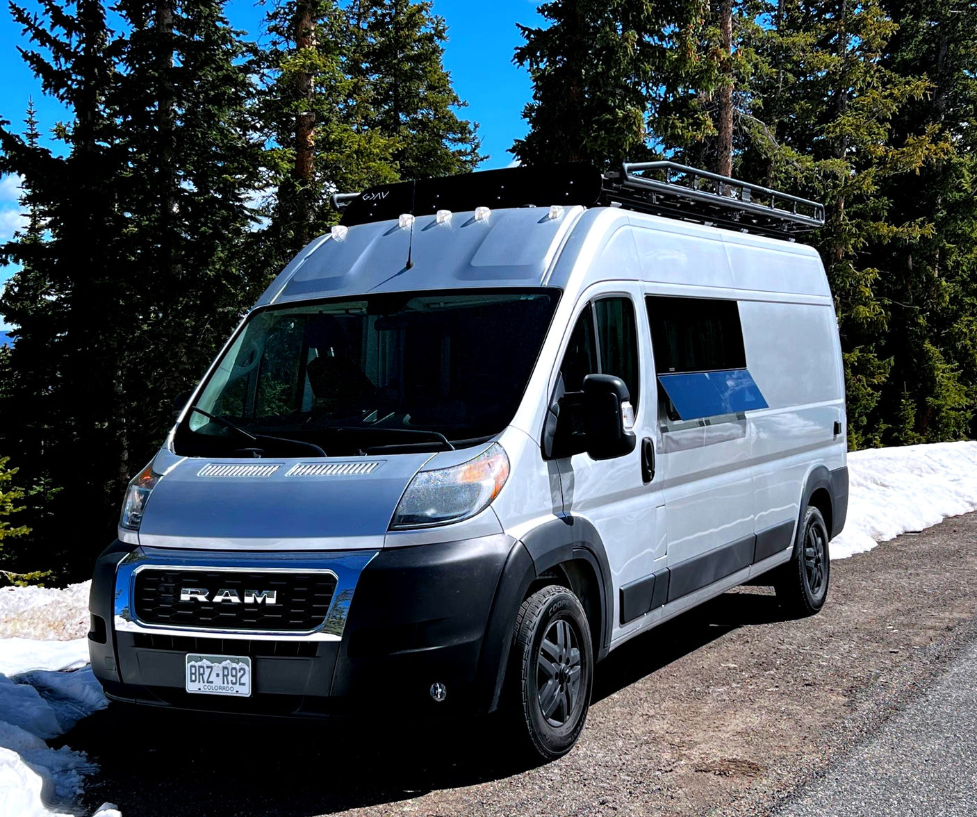 A white Ram camper van, equipped for adventure, parked in snowy mountains. Consider this RV rental for your next trip.