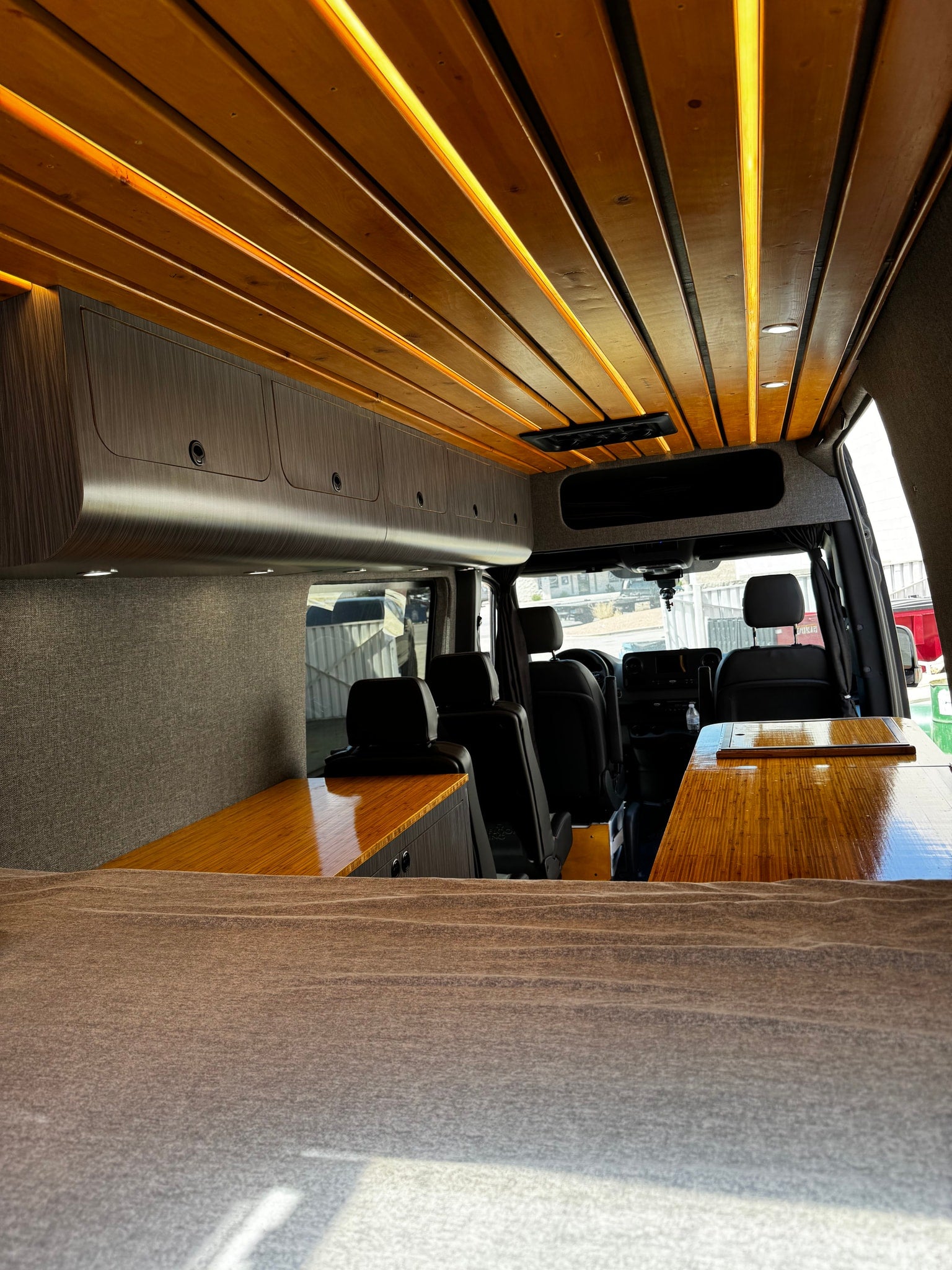 Stylish RV rental camper van interior: wood ceiling, ambient lighting, custom storage, & sleek wood tables.