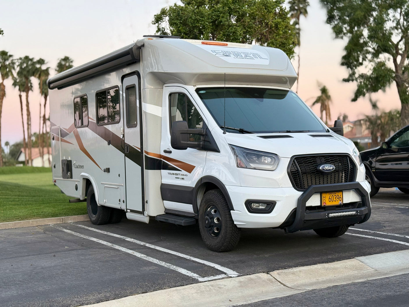 White Coachmen Cross Trail RV rental, a Ford Transit-based motorhome with a front brush guard, is parked. Ready for travel adventures.