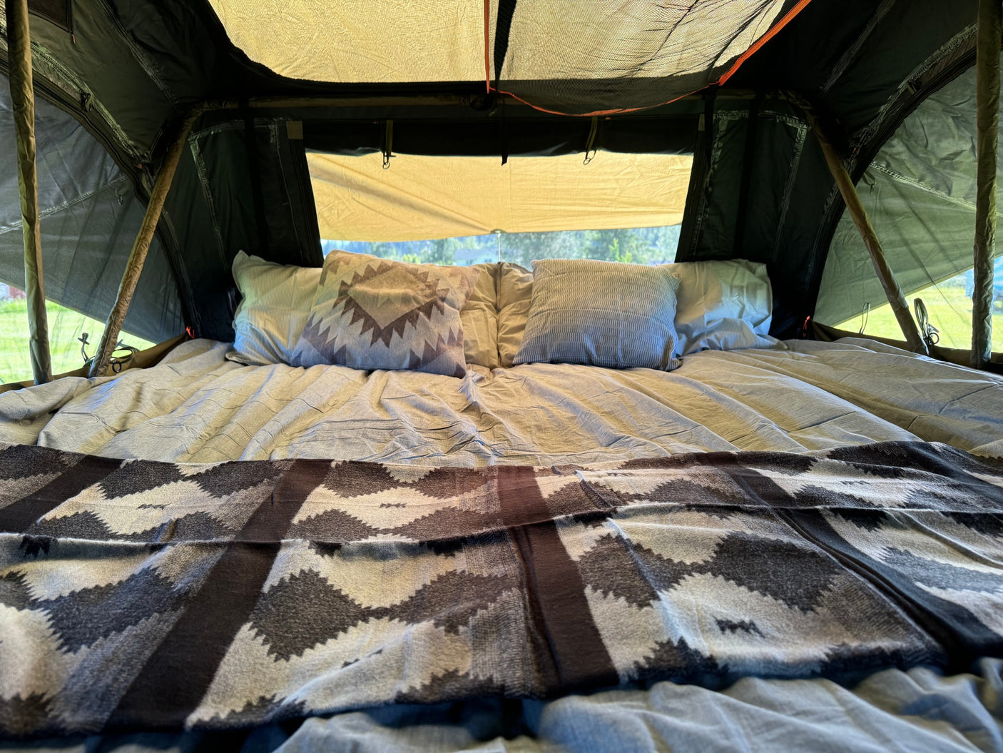Cozy bed set up inside a tent with pillows and patterned blanket, ready for an RV rental adventure.