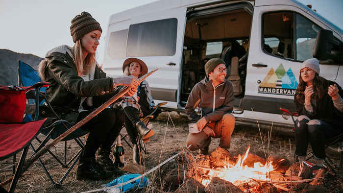 Friends enjoy a campfire by their WanderVan RV rental. An ideal setting for outdoor adventures & memorable moments.