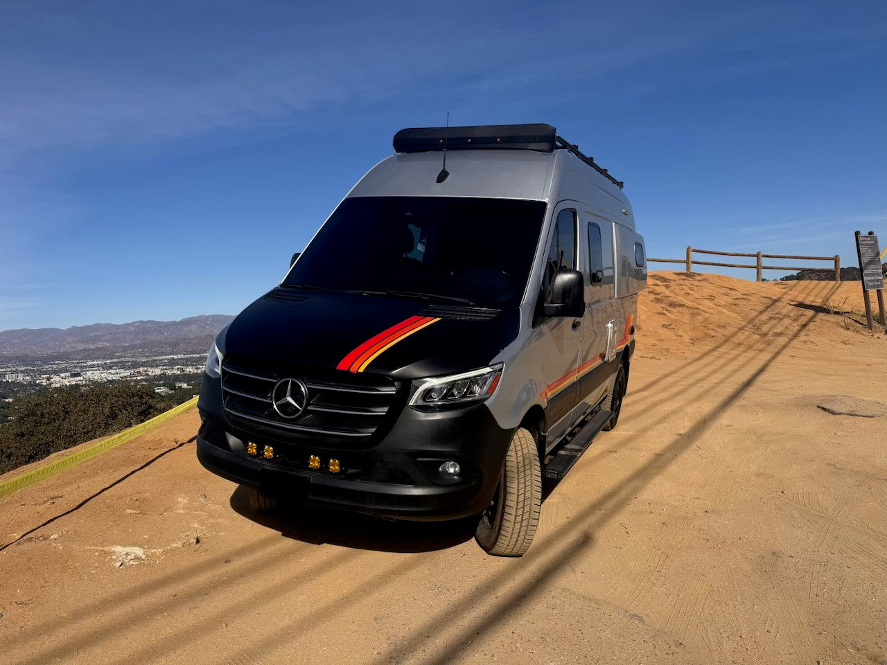 Stunning Mercedes Sprinter adventure van, ideal for your next RV rental journey. Parked on a scenic dirt hill overlooking a city.