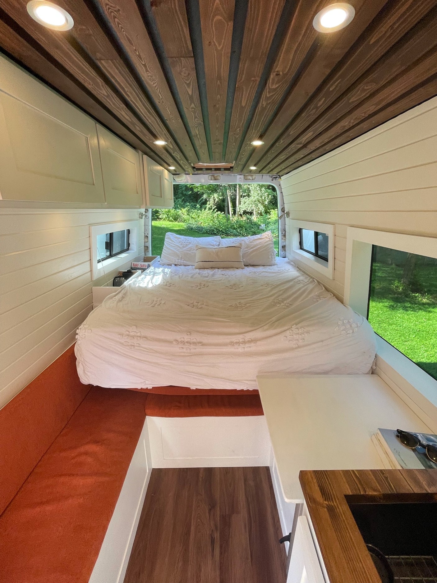 Bright RV rental interior featuring a large bed, full kitchenette, and comfortable seating in a well-designed camper van.