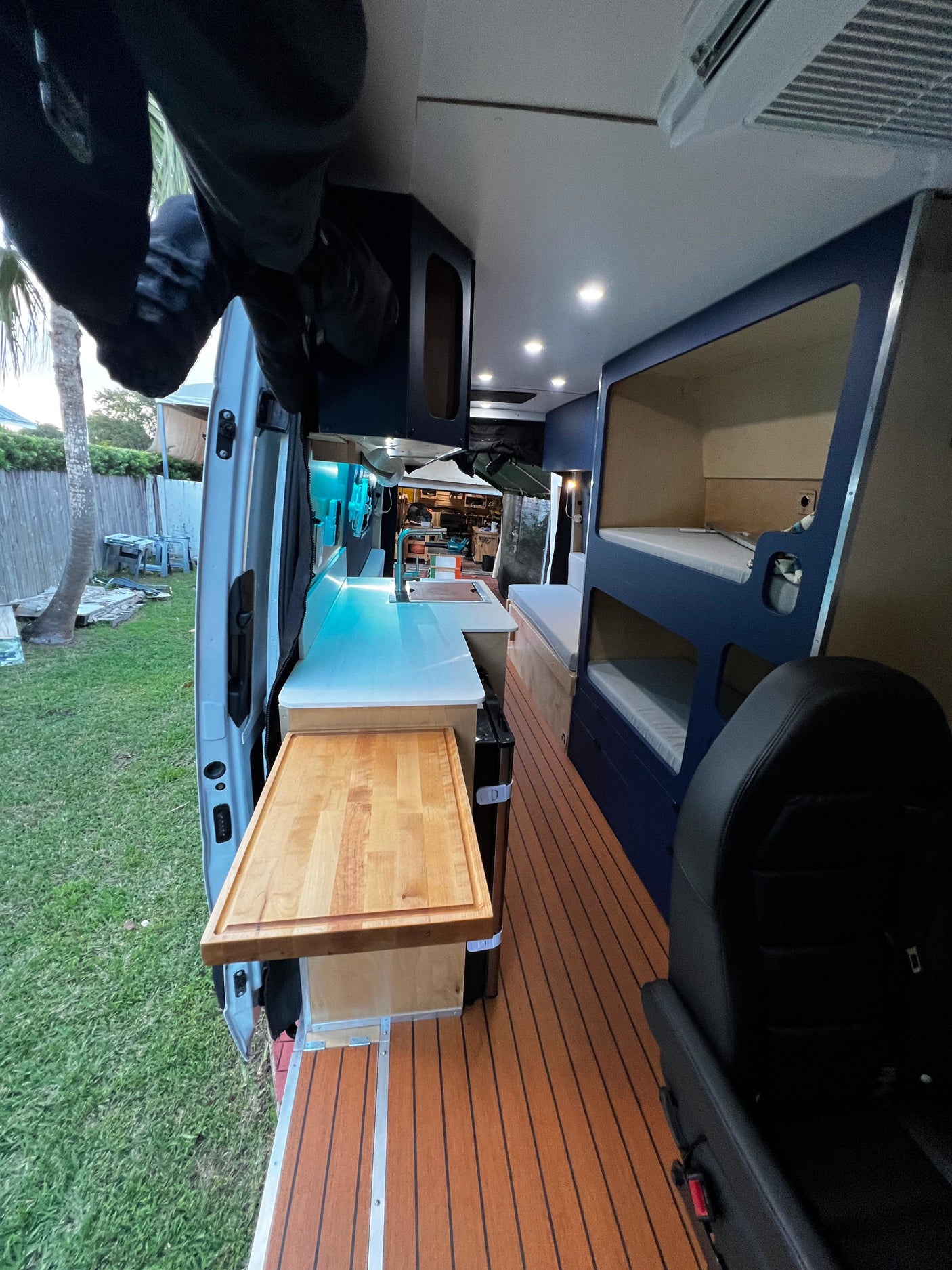 Inside a modern RV rental: cozy kitchen, bunk beds, and wood flooring visible from the open door to a backyard.