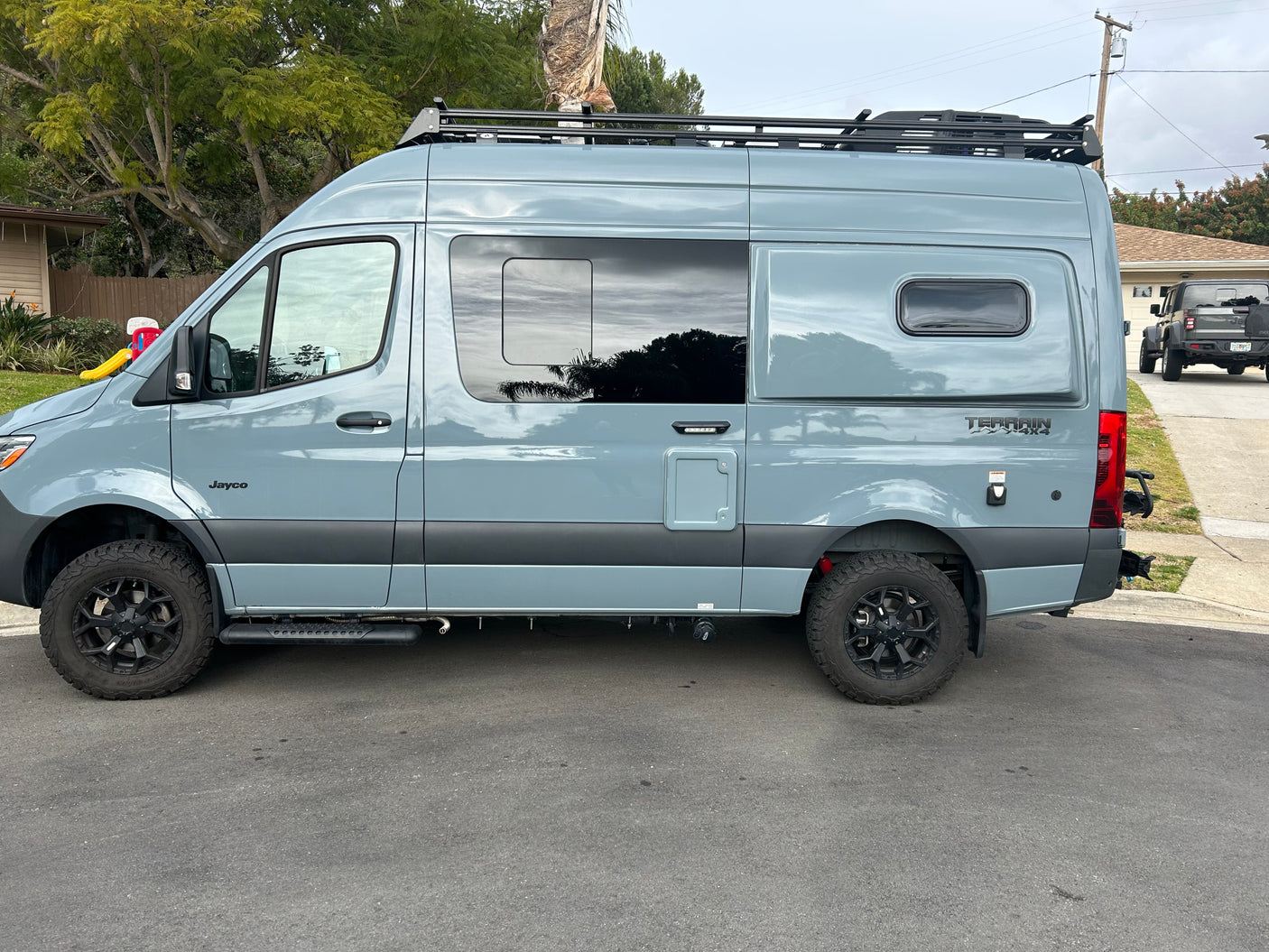 This gray Jayco Terrain 4x4 camper van, a perfect rv rental, boasts rugged tires & a roof rack.
