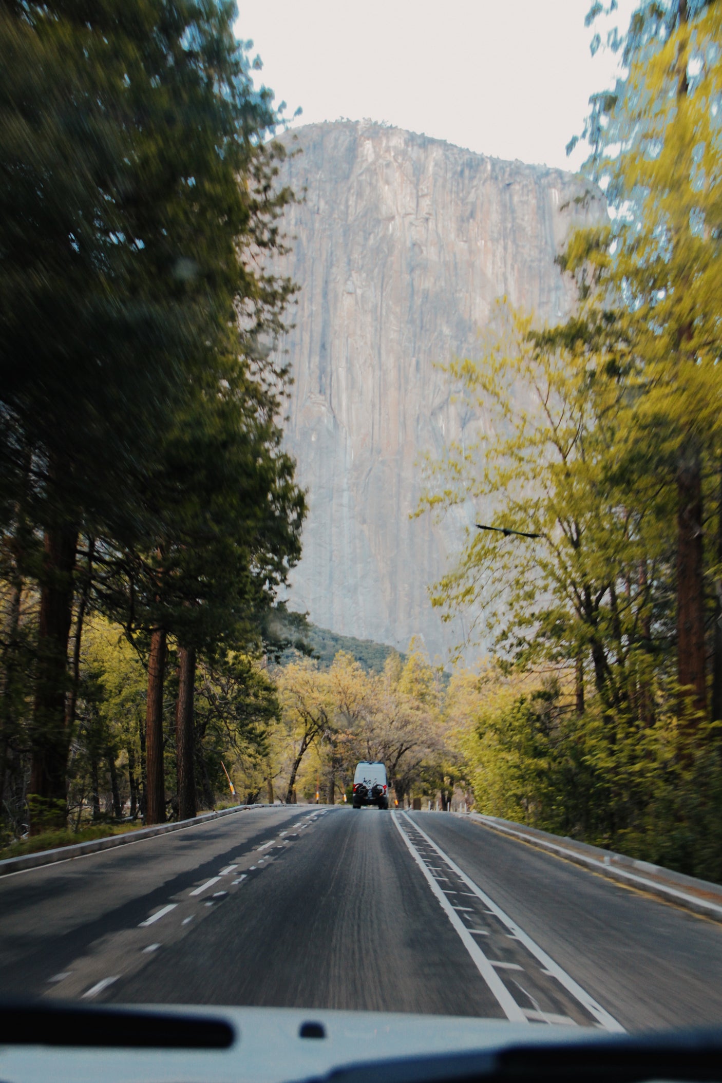 An RV rental travels a winding road through lush forests, leading to a massive rock face in a stunning natural valley.