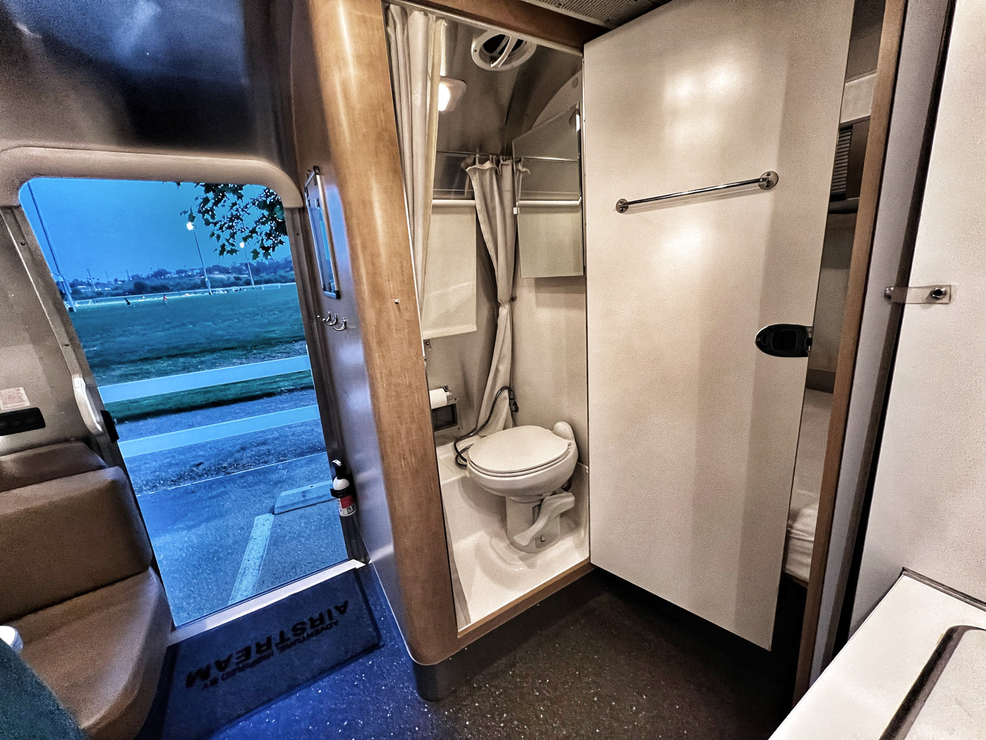 Inside an RV rental: compact bathroom with toilet, shower, and open door view of a field. Perfect for travel adventures.