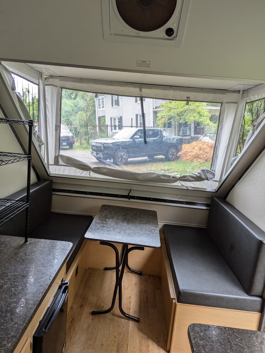 Inside an RV rental, this A-frame camper features a cozy dining area with a clear window view of a truck.