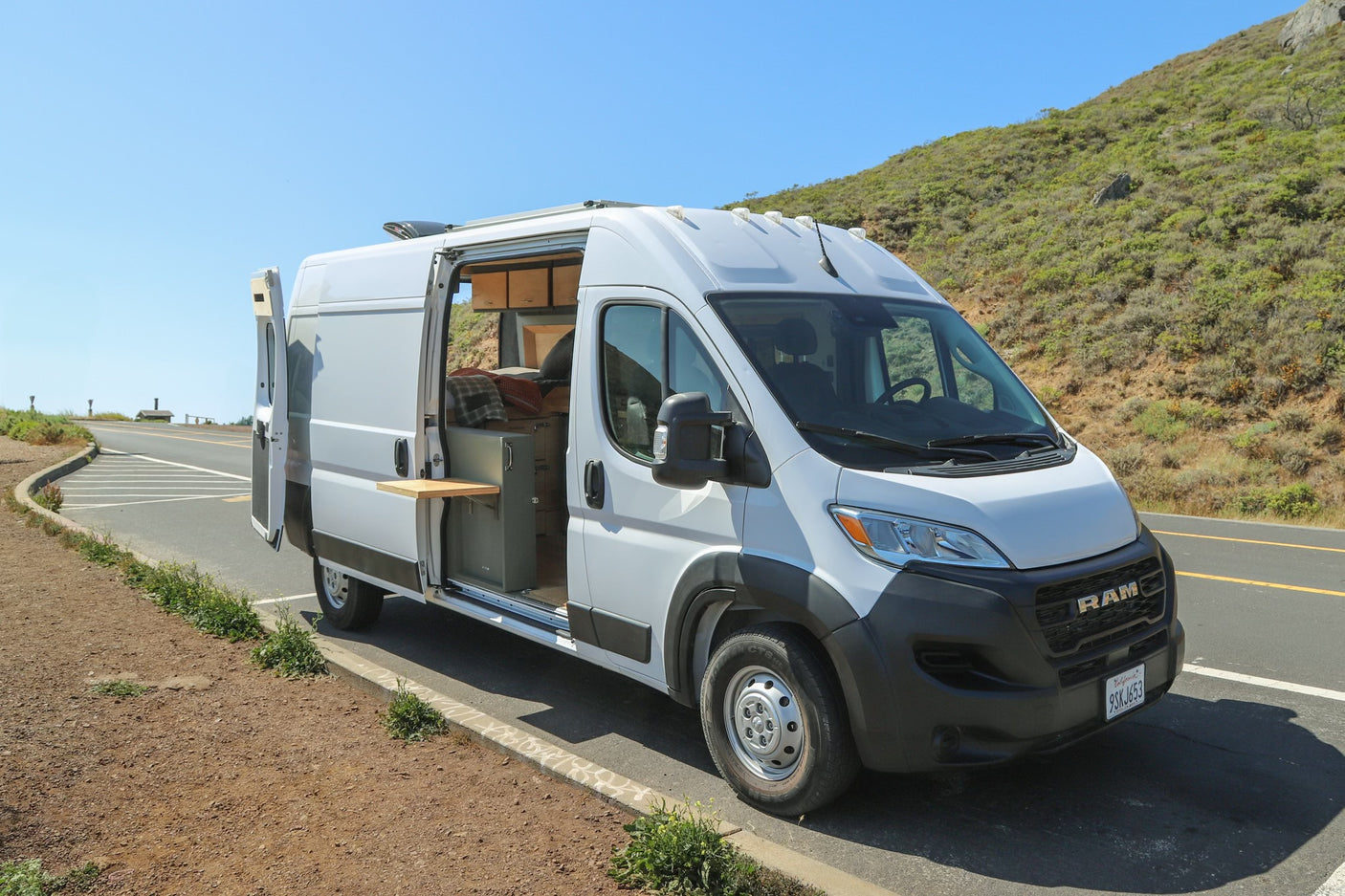 White Ram ProMaster campervan, an ideal RV rental, parked roadside with side door open, revealing its custom interior. Perfect for road trips.