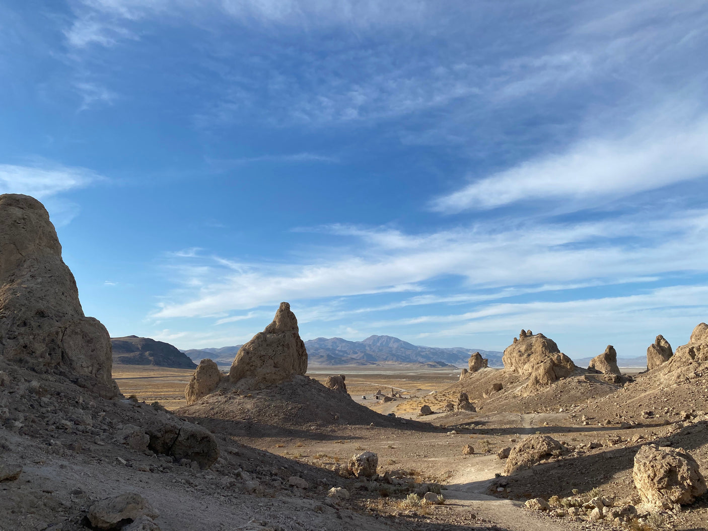 Explore a striking desert landscape with towering tufa formations, distant mountains, and a dirt path. Ideal for an RV rental adventure!