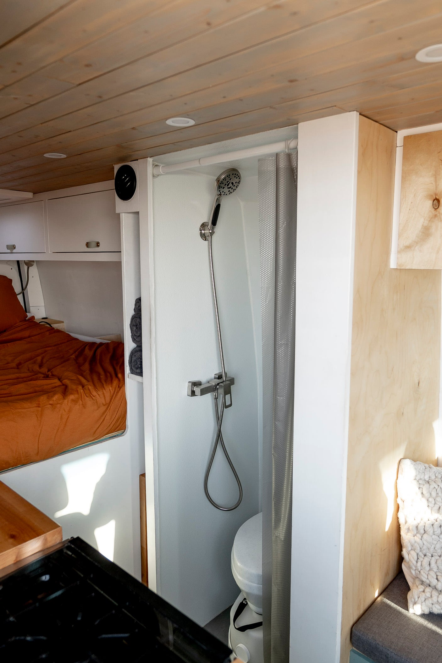 Compact RV rental interior with a functional shower, composting toilet, bed, and integrated kitchen setup. Ideal for road trips.