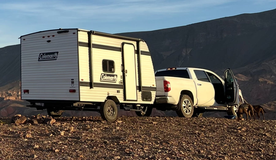 Adventure awaits with this Coleman RV rental! A white truck tows a travel trailer on a rocky hill with dogs and mountains.|RV rental floor plan: bed