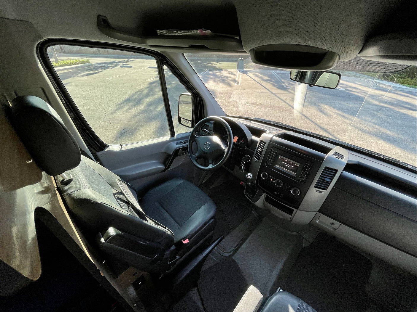 Driver's cabin of an RV rental, showing steering wheel, dashboard, and bright view out the windshield.