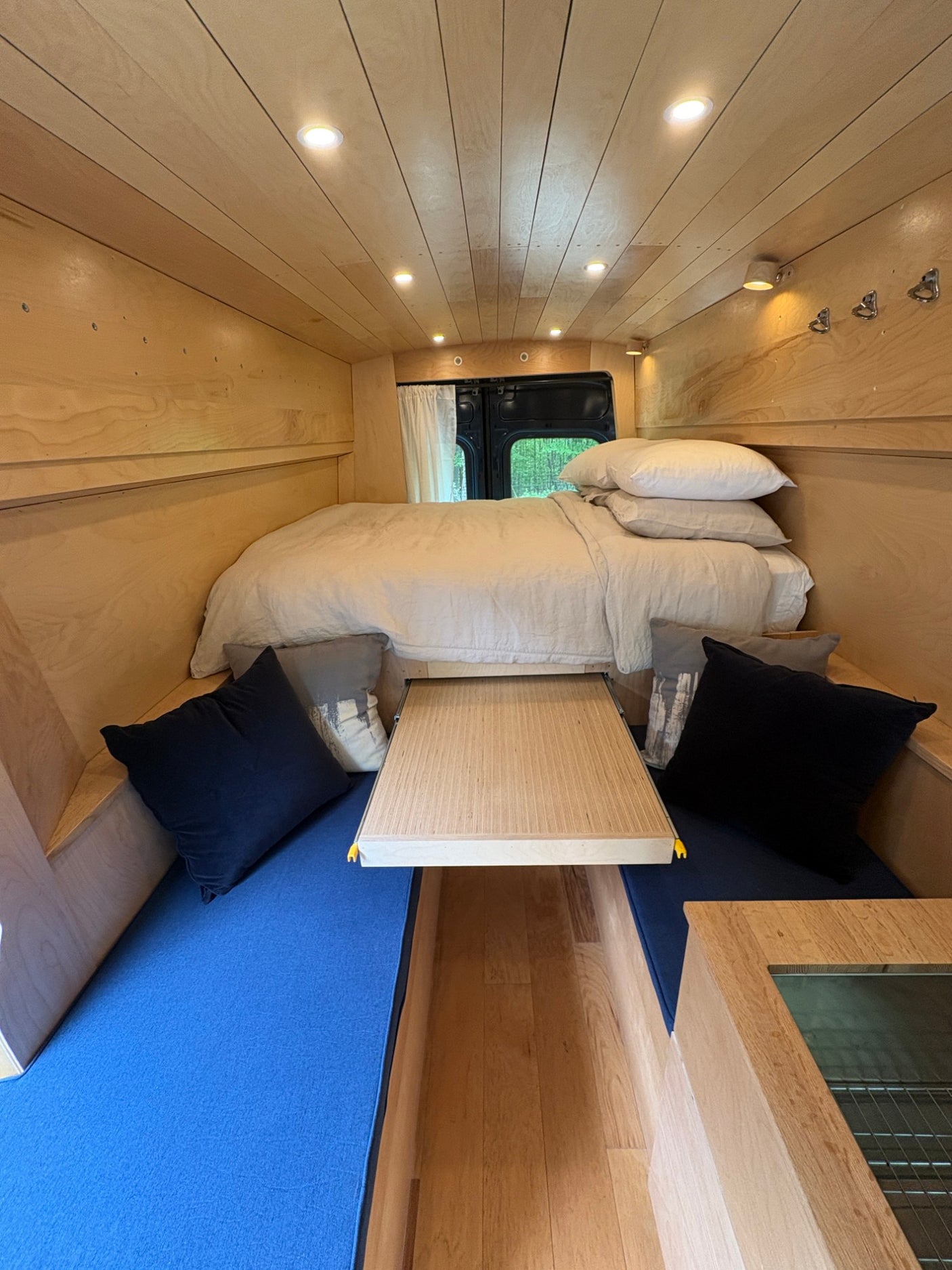 Cozy RV rental interior: wood-paneled walls, bed, dining area with blue cushions. Ideal for travel.