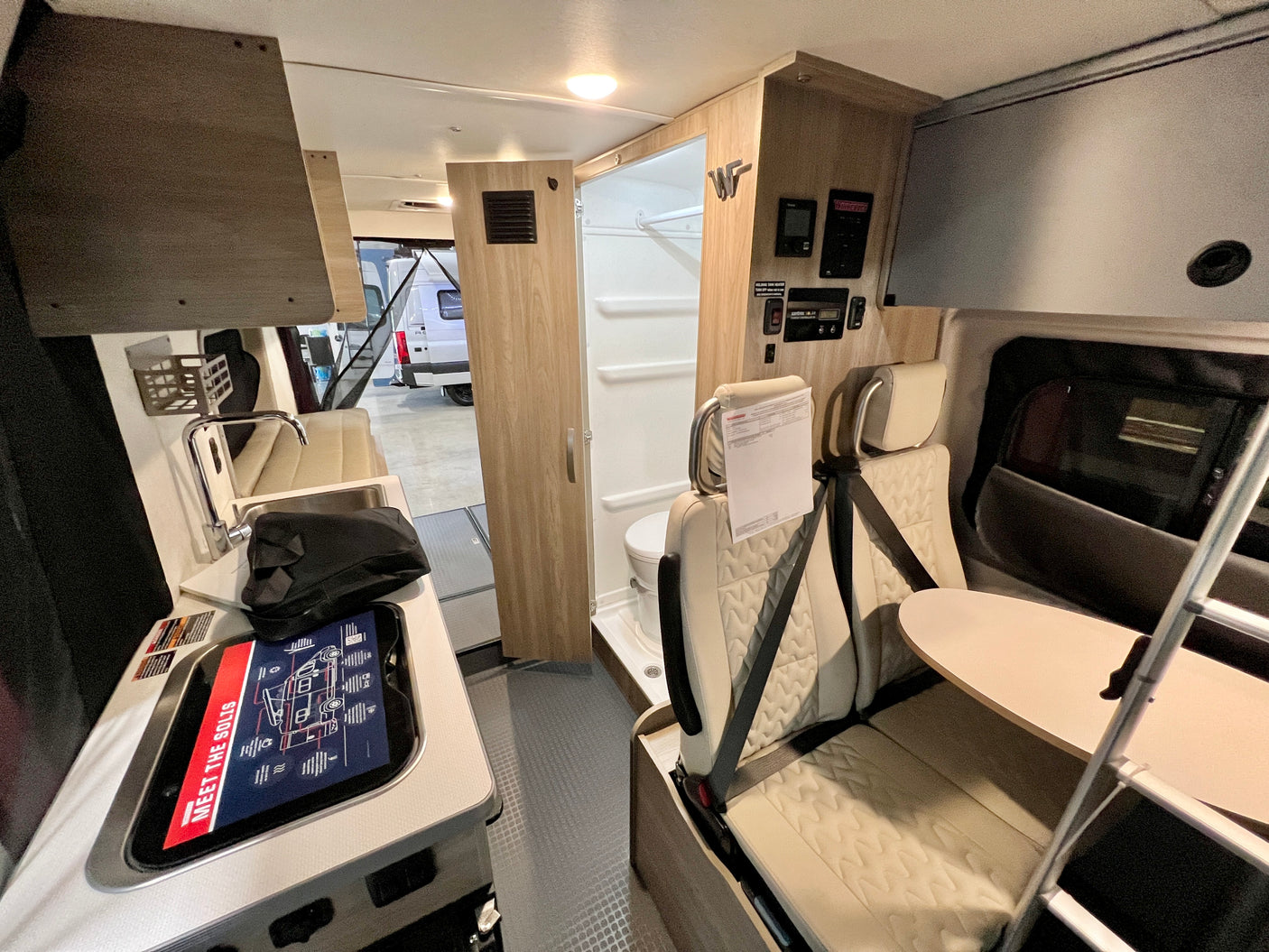 Modern Winnebago Solis camper van interior for rv rental, showing kitchen, bathroom, and seating with table.