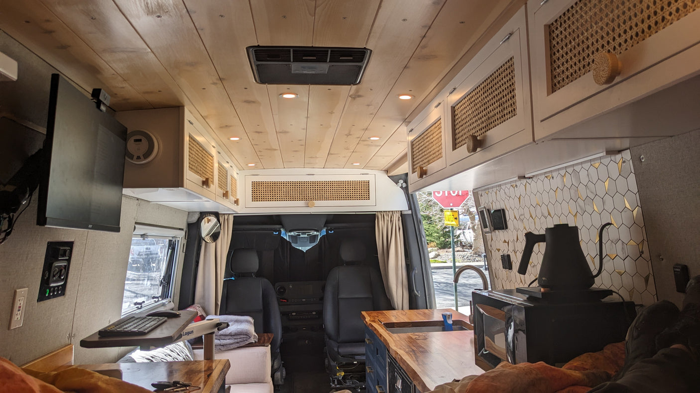 Inside a stylish camper van, great for an RV rental. View towards the front with a kitchen, workspace, and wooden ceiling.