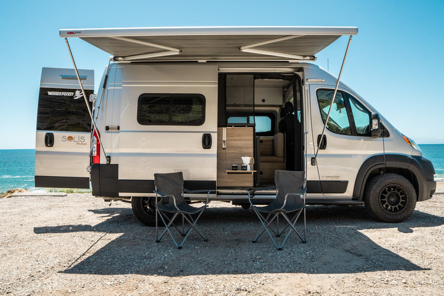 Enjoy this Winnebago Solis Pocket camper van for your next RV rental, featuring an awning & chairs by the ocean.