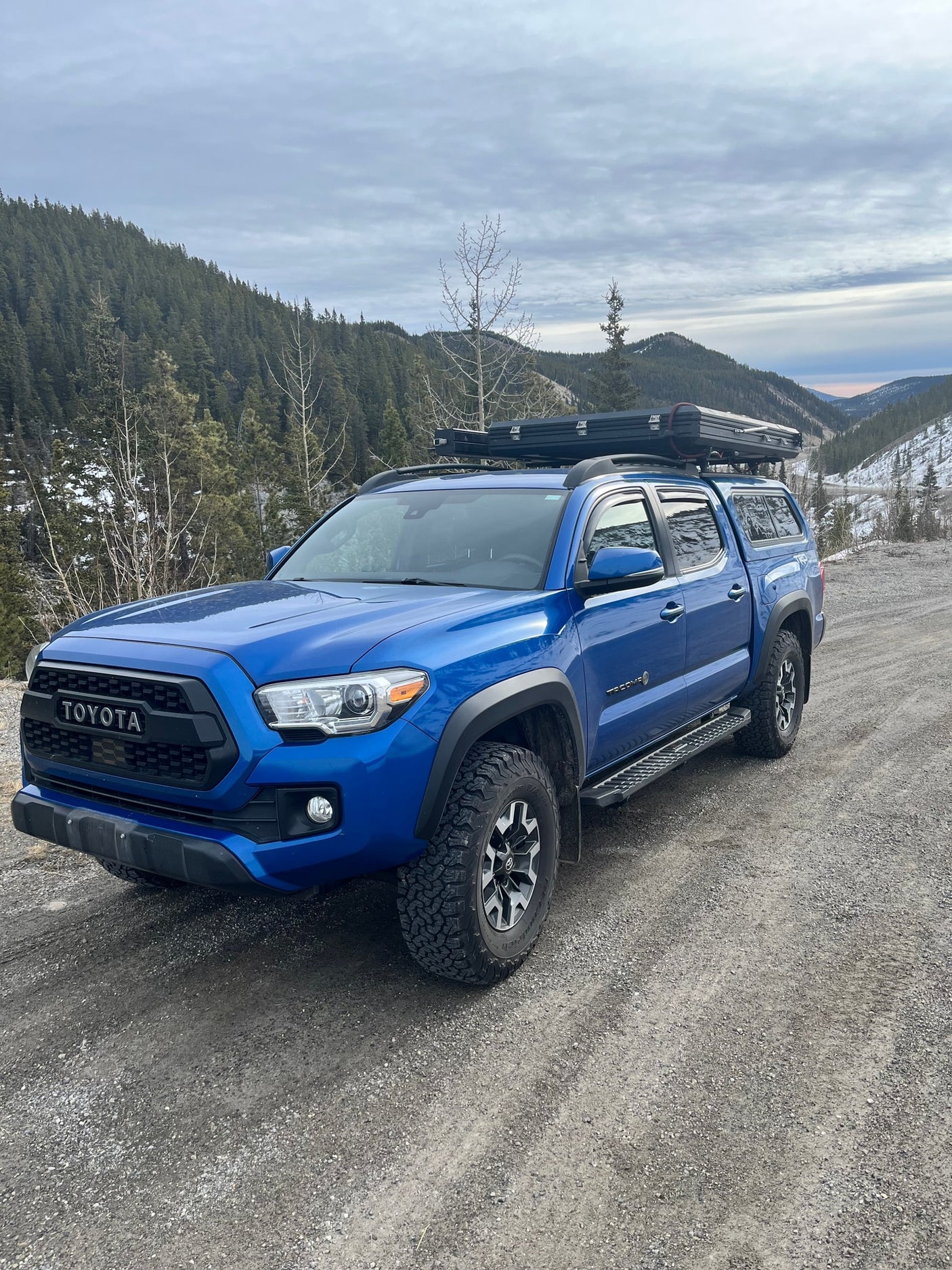 Blue Toyota Tacoma with rooftop tent parked on a mountain gravel road. Get ready for off-road adventure, an ideal RV rental alternative.