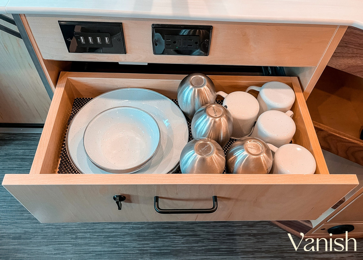 RV rental kitchen drawer open, revealing stacked plates, bowls, and metal cups. USB ports & power outlets above.