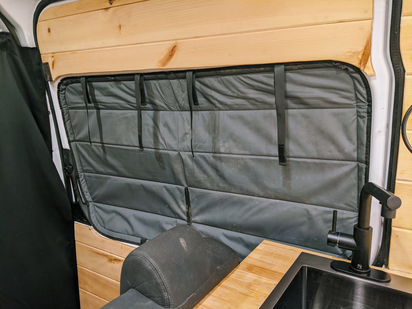 Cozy RV rental interior featuring wood walls, padded window insulation, kitchen sink with faucet, & comfy seating. Ideal for travel.