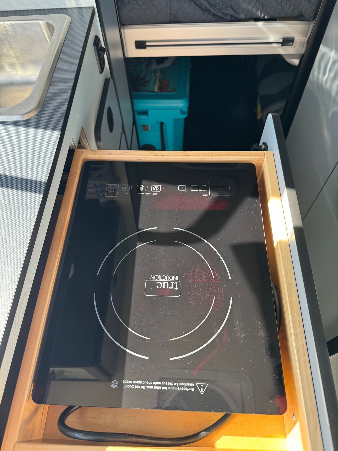 Compact kitchen features: A pull-out induction cooktop in an RV rental setup, beside a sink.